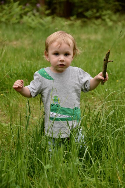 baby in long grass holding a stick